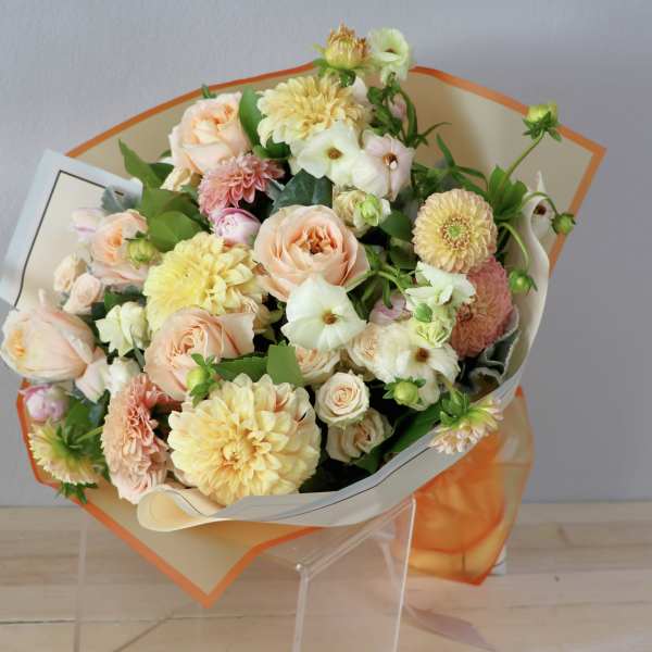 Bouquet of peach roses and pale yellow dahlias wrapped in cream and orange paper