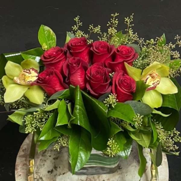 Red roses with pale green orchids in a low vase arrangement