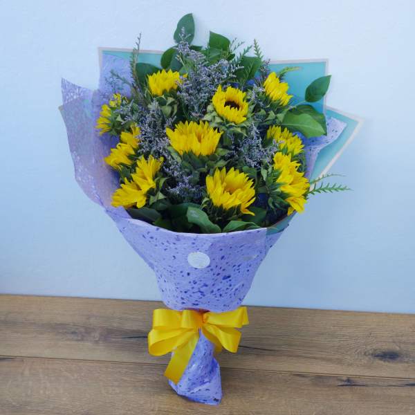 Bouquet of yellow sunflowers wrapped in purple paper with a yellow ribbon