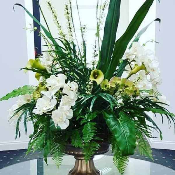 Tall floral arrangement with white orchids and green calla lilies in a pedestal vase