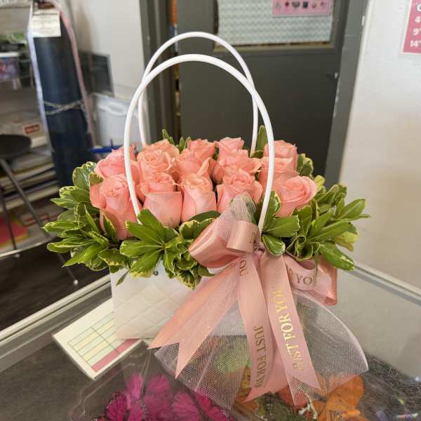 Pink roses arranged in a white handled gift basket with a pink ribbon