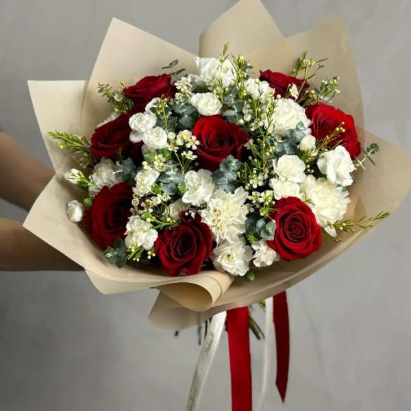 Bouquet of red roses and white carnations wrapped in beige paper