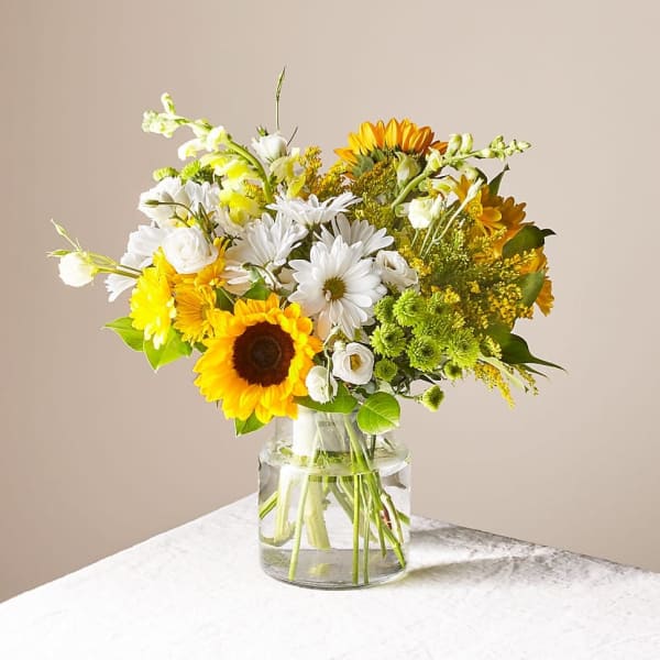 Bouquet of sunflowers, white daisies, and yellow blooms in a clear glass vase