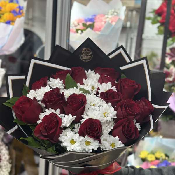 Bouquet of red roses and white daisies wrapped in black paper