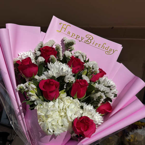 Bouquet of red roses and white flowers in pink wrapping with a Happy Birthday card