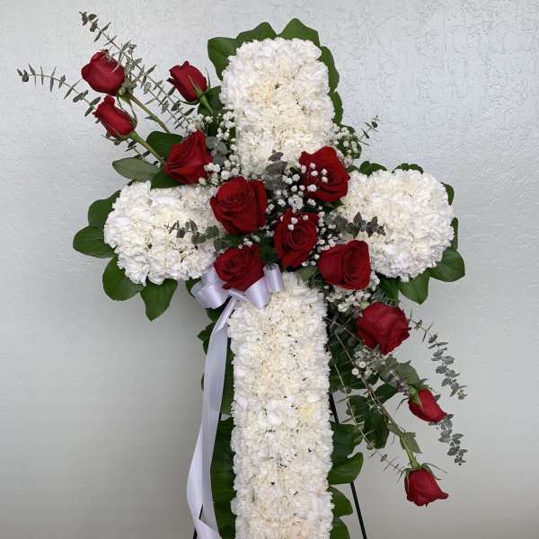Cross-shaped floral tribute with red roses and white carnations on a stand