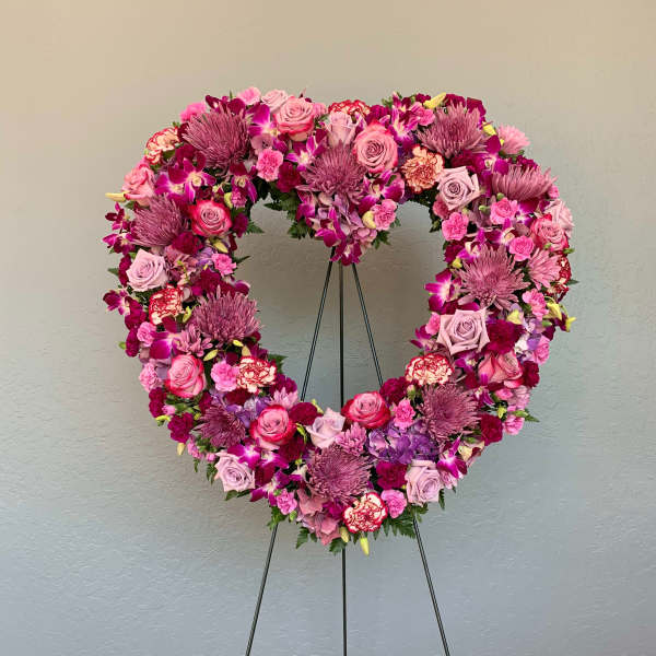Heart-shaped floral wreath on a stand with pink and purple flowers