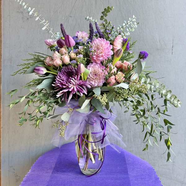 Mixed pink and purple bouquet in a clear glass vase with trailing greenery
