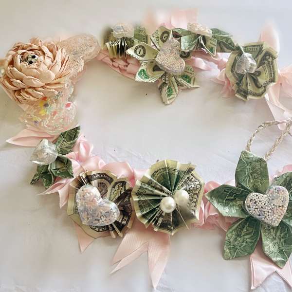 Money lei with pink ribbon and paper flowers on a white surface