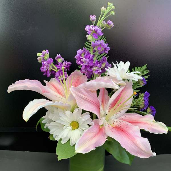 Pink lilies and white daisies in a green vase with purple flowers