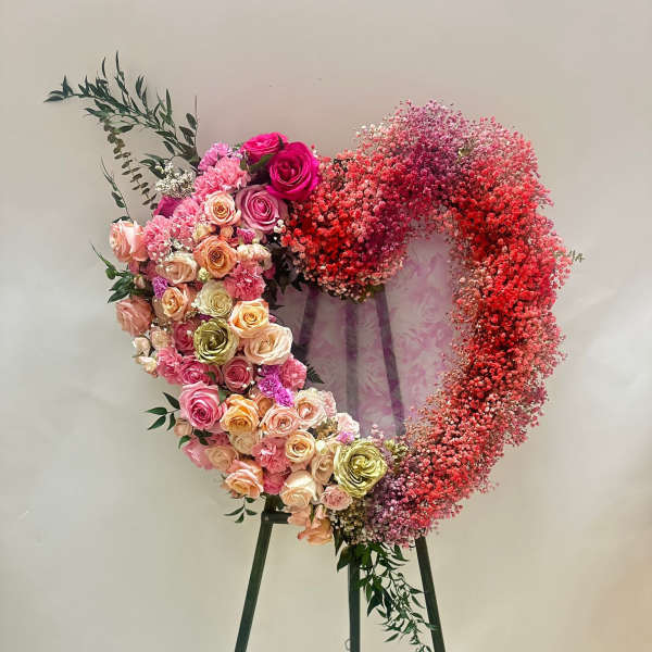Heart-shaped floral wreath on a stand with pink and red roses