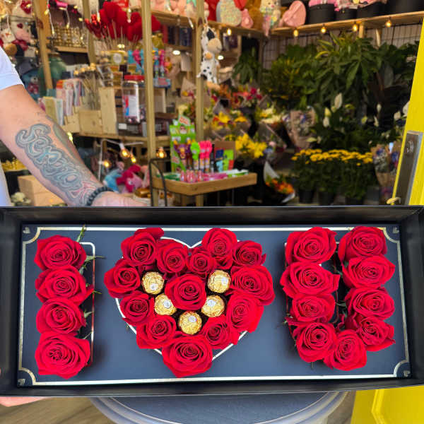 Red roses arranged as the word "I" with a heart and "U" in a gift box