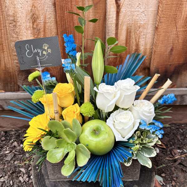 Mixed bouquet with white and yellow roses, a green apple, and blue accents in a wooden box