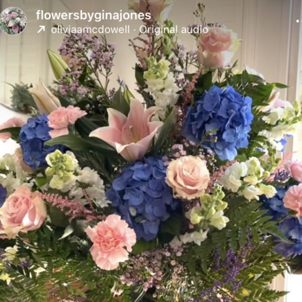 Large mixed bouquet in a clear glass vase with pink roses, blue hydrangeas, and lilies