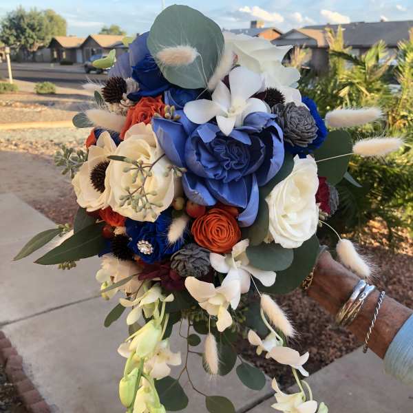 Handheld bouquet with blue, white, and orange flowers and trailing orchids