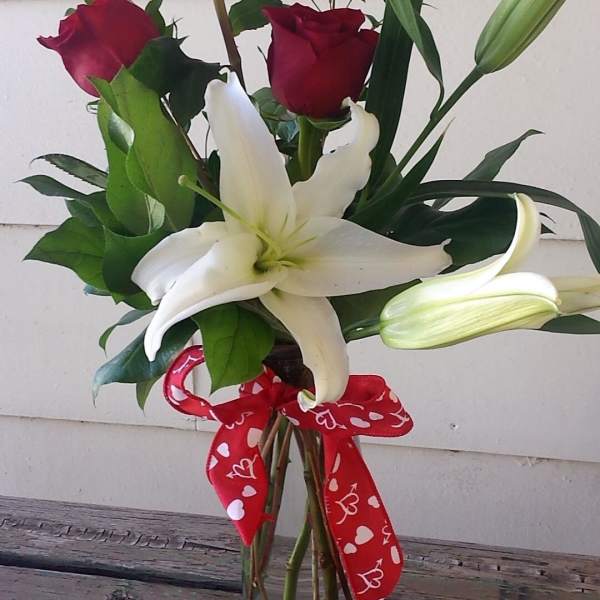 Red roses and a white lily in a glass vase with a heart ribbon