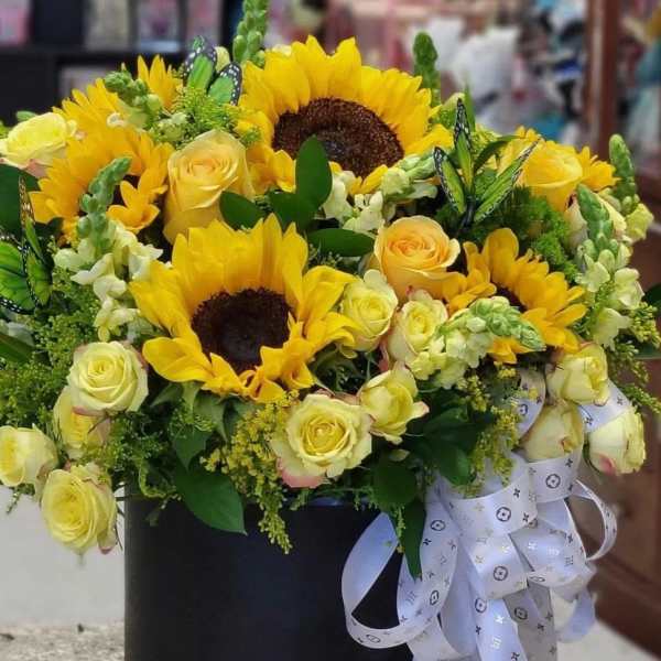 Yellow sunflowers and roses arranged in a black box with a white ribbon.