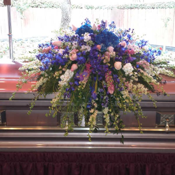 Large floral spray on a casket with blue, purple, pink, and white flowers