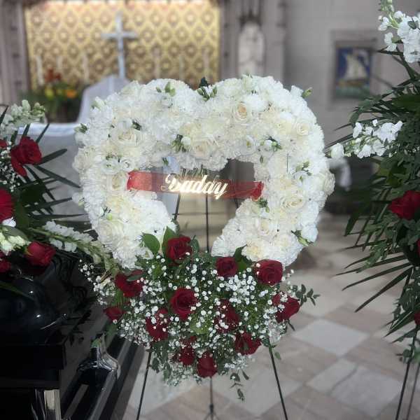 Heart-shaped white floral wreath with red roses and a ribbon on an easel