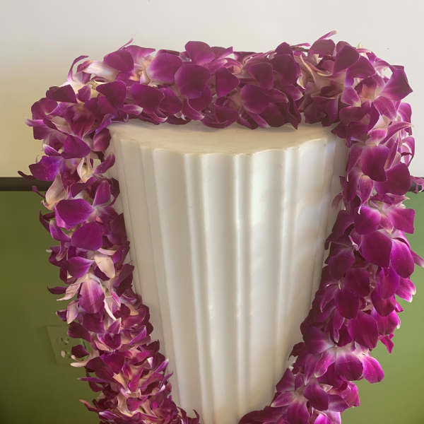 Purple orchid lei draped over a white pedestal vase
