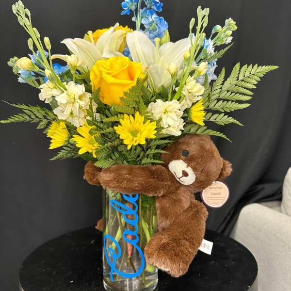 Bouquet of yellow and white flowers in a glass vase with a teddy bear