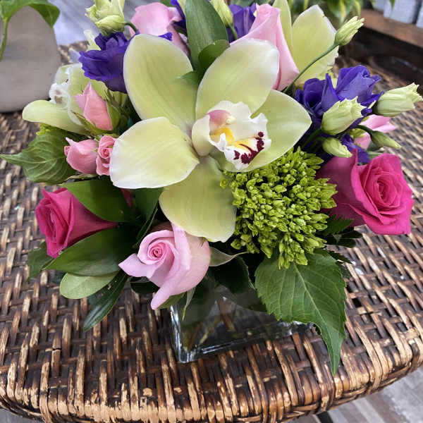 Bouquet of pink roses, purple lisianthus, and a pale orchid in a glass vase