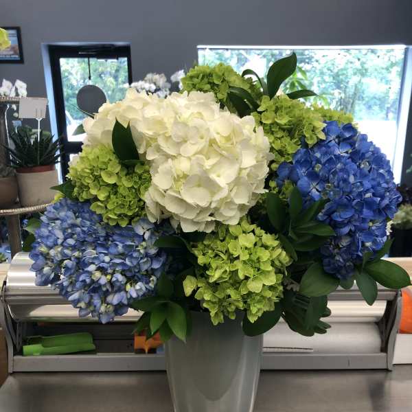 Blue, green, and white hydrangea arrangement in a tall gray vase