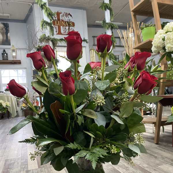 Red roses arranged in a clear glass vase with greenery