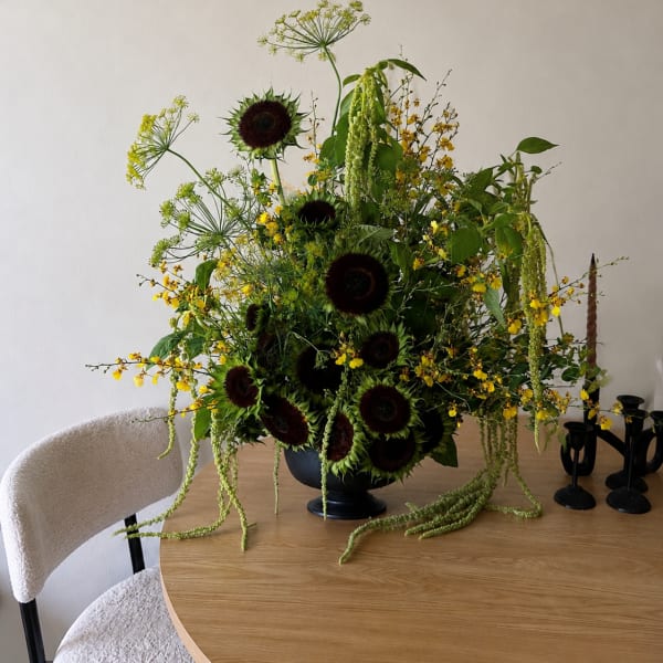 Large floral arrangement with dark sunflowers and yellow blooms in a black vase
