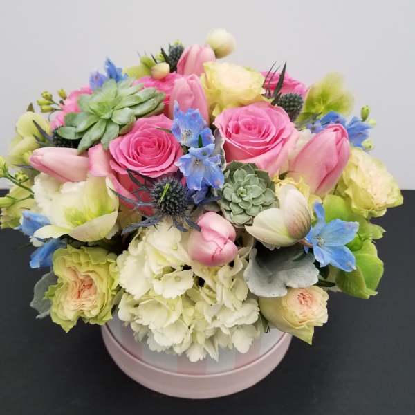 Pink and cream bouquet with roses, tulips, and blue accents in a round box