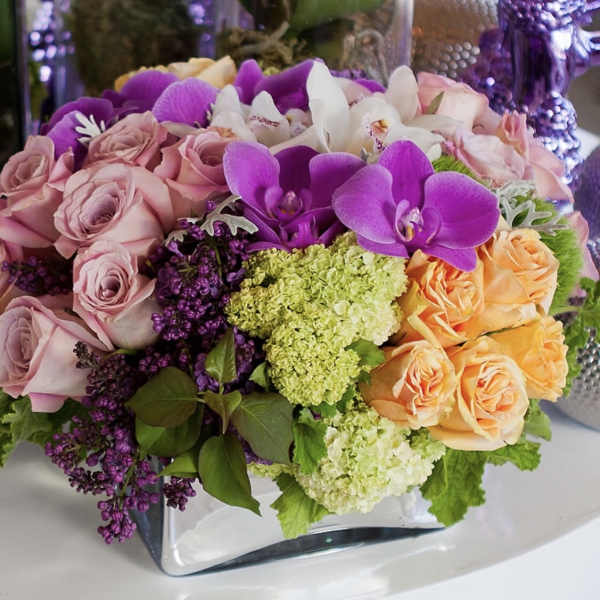 Mixed bouquet of pink roses, purple orchids, and white flowers in a glass vase