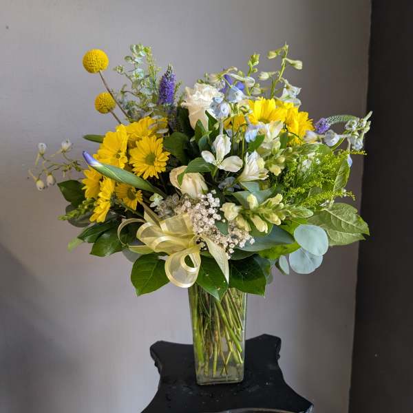 Yellow and white mixed bouquet in a clear glass vase with a ribbon