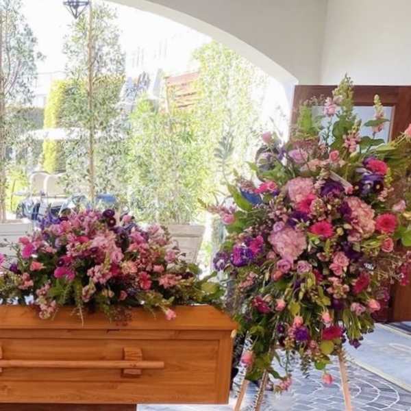 Floral casket spray with pink, purple, and white flowers beside an open casket
