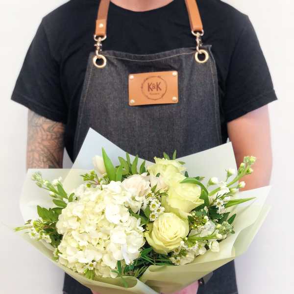 Handheld bouquet of white and pale yellow flowers wrapped in paper