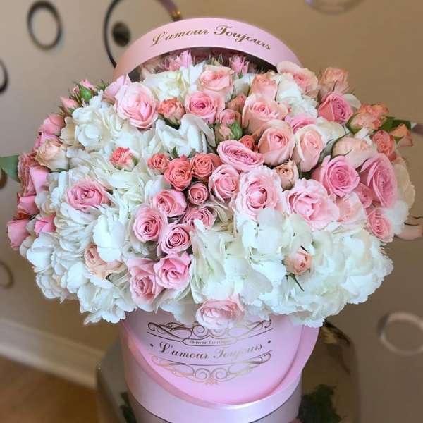 Round hatbox arrangement of pink roses and white flowers in a pink box.