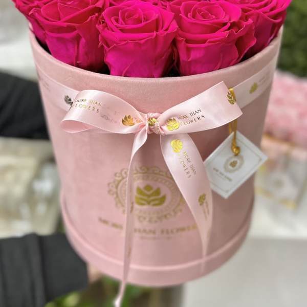 Hot pink roses arranged tightly in a round pink hat box with ribbon and logo