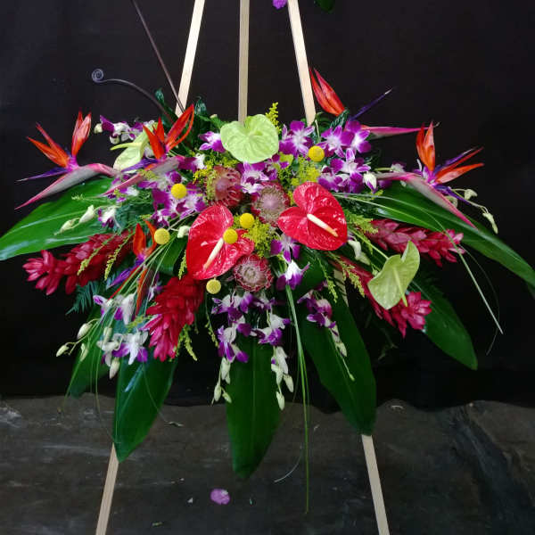 Tall tropical floral standing arrangement on an easel with purple, red, and white blooms
