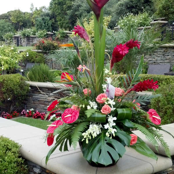 Tall tropical floral arrangement with red blooms and pink roses in a black vase