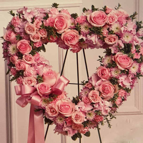 Heart-shaped pink rose and mixed flower wreath on a stand with a satin ribbon