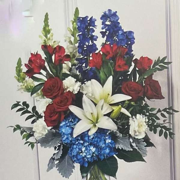 Bouquet of red roses, white lilies, blue flowers, and greenery in a clear vase