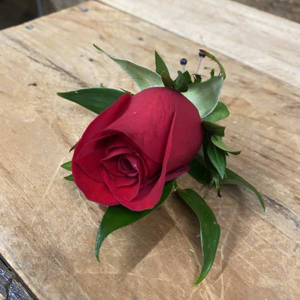 Single red rose boutonniere with green leaves on a wooden surface