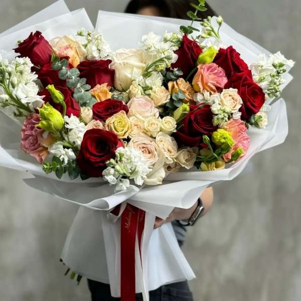 Handheld bouquet of red, cream, and pink roses wrapped in white paper