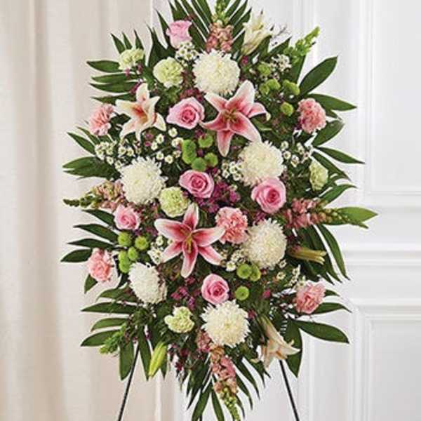 Standing floral spray with pink lilies, roses, and white blooms on an easel