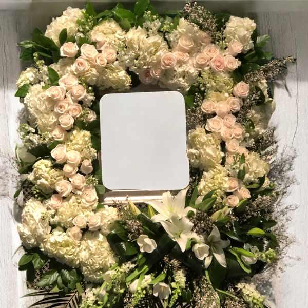 Floral wreath with pale roses, hydrangeas, and white lilies around a blank center panel