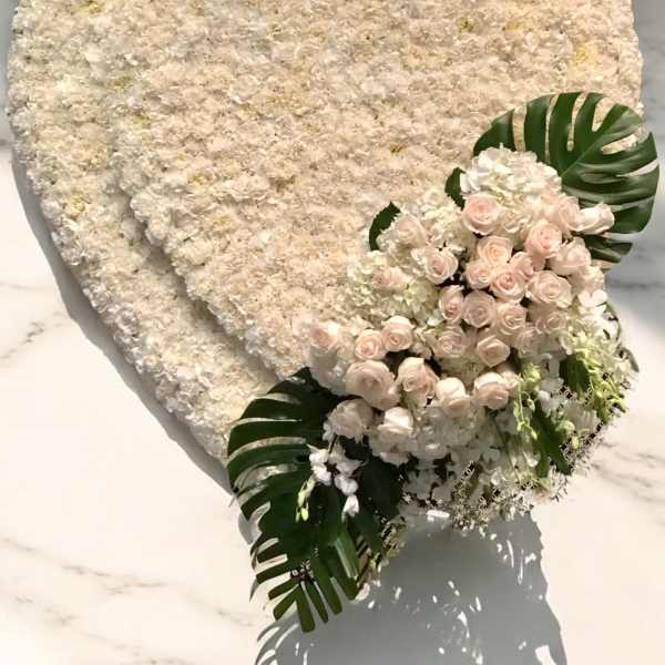 Heart-shaped white floral arrangement with pale pink roses and tropical leaves
