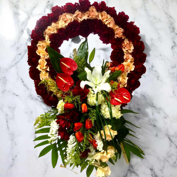 Floral wreath with red and peach roses, white lilies, and red anthuriums