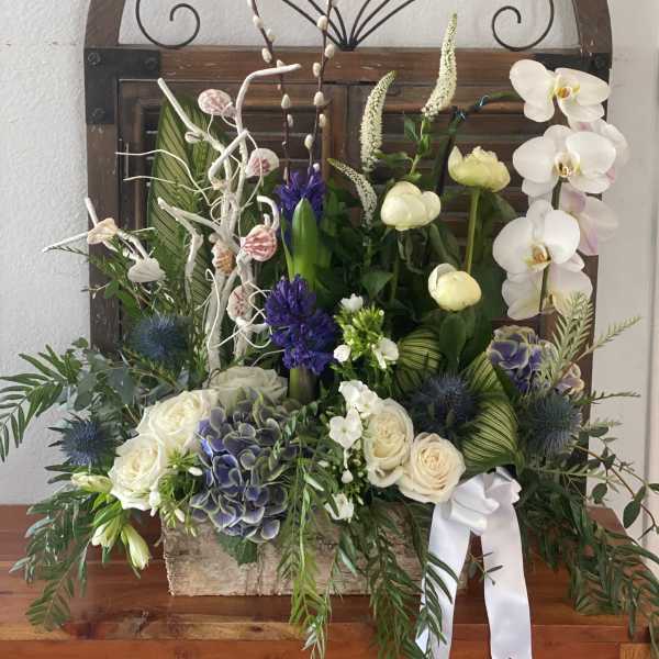 Mixed floral arrangement with white orchids, roses, and blue thistles in a wooden container