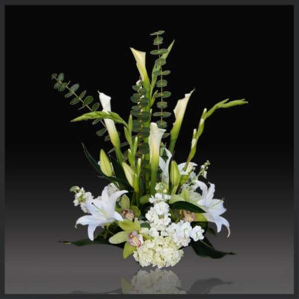 Tall white lily arrangement with green foliage on a dark background