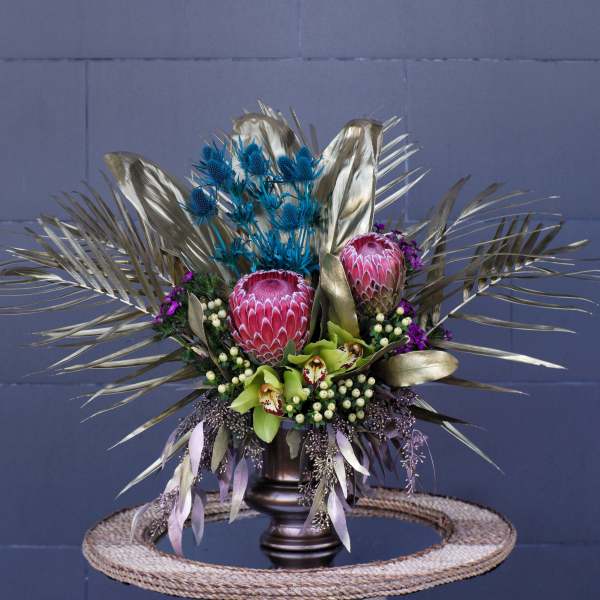 Tropical bouquet with pink protea and blue thistle in a dark vase