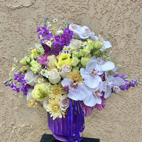 Mixed bouquet in a purple vase with orchids, roses, and daisies